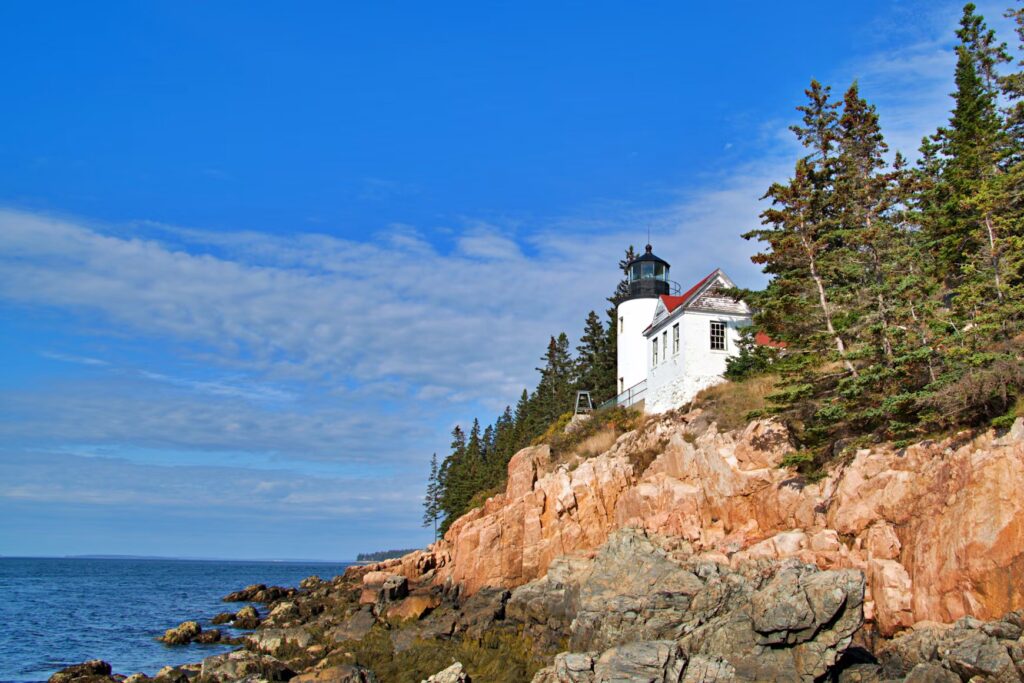 Bass Harbor Head Light perched on a steep, rocky granite cliff face overlooking the ocean.