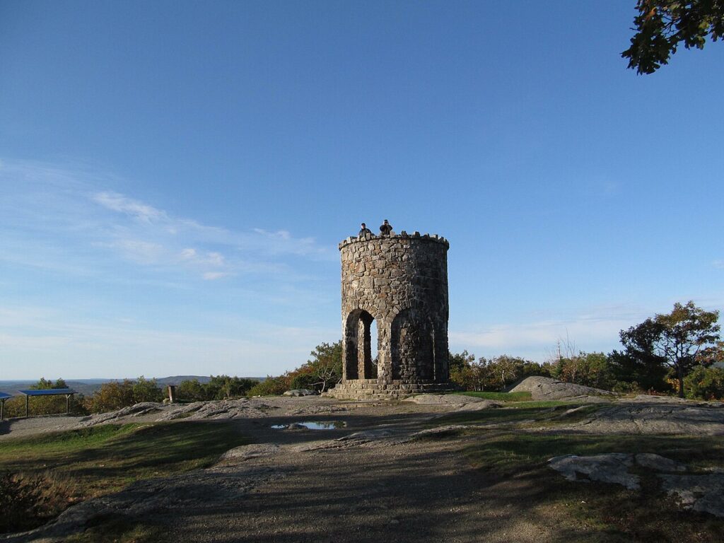 The historic stone memorial tower standing on the summit of Mount Battie under a clear blue sky.