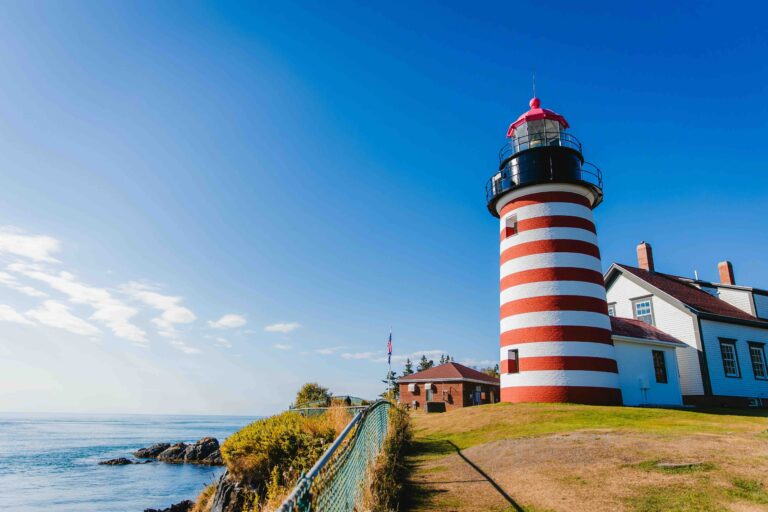 25 Best Things to Do in Maine (Must-Do Activities & Hidden Gems) A classic red and white striped lighthouse on a rocky cliff overlooking the ocean, representing the best things to do in Maine.