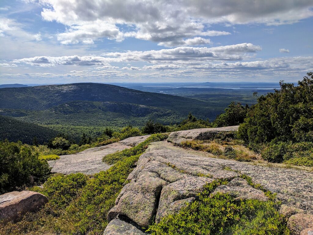 Wide, panoramic mountain view looking out over green forests from a high, rocky granite ledge.