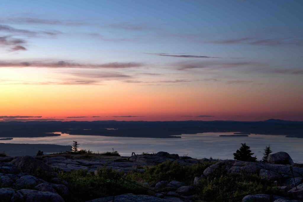 A vibrant, colorful sunset sky stretching over the ocean islands seen from a high rocky summit.