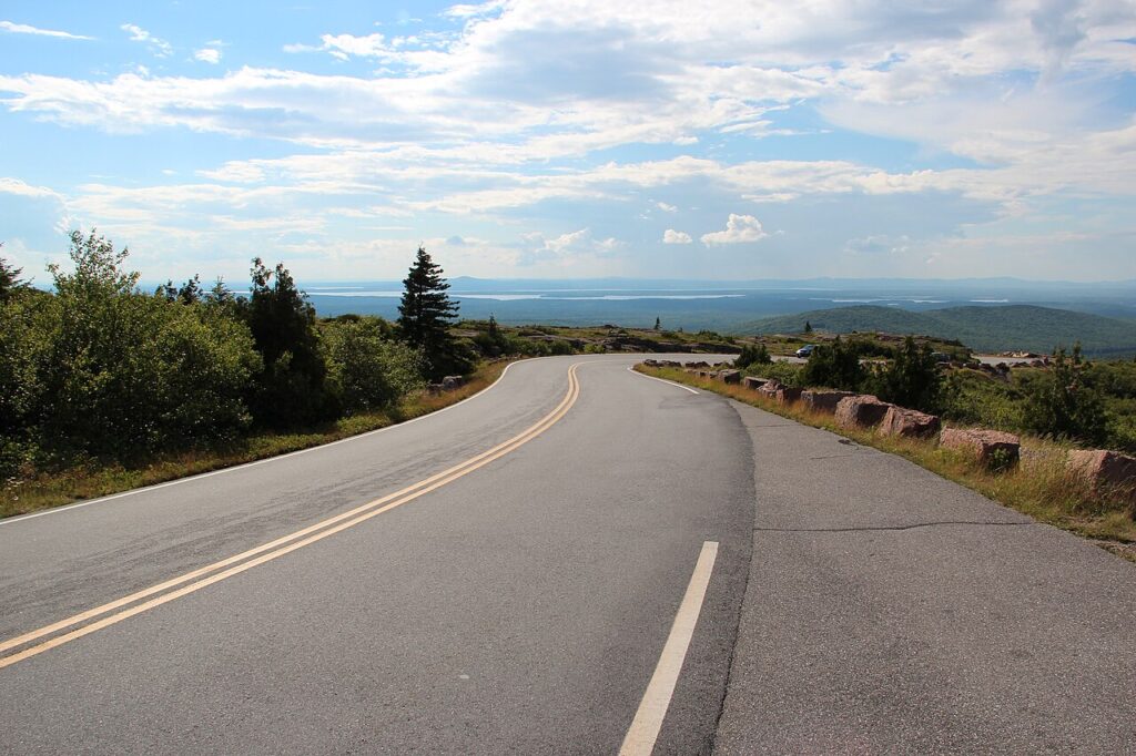 A paved road winding uphill through a scenic mountain landscape toward a distant view.