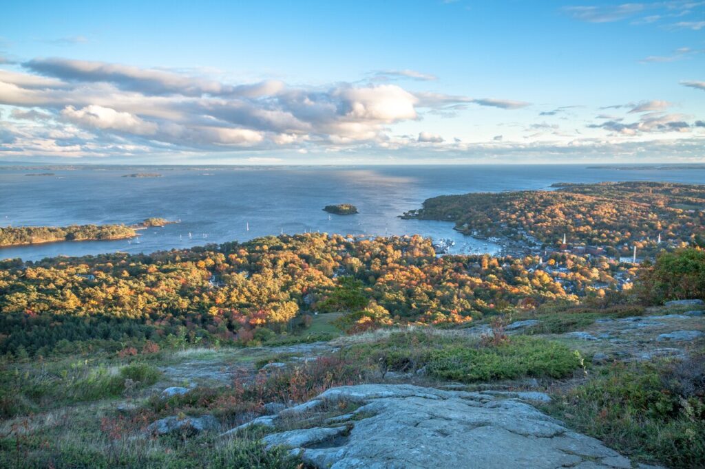 A sweeping view of Camden Harbor and the coastal islands framed by colorful autumn trees on the hillside.