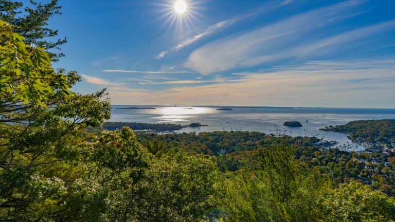 15 Best Things to Do in Camden, Maine (Mountains & Sea) Sun shining over the scenic Penobscot Bay viewed from a forested hilltop, showcasing best things to do in Camden.