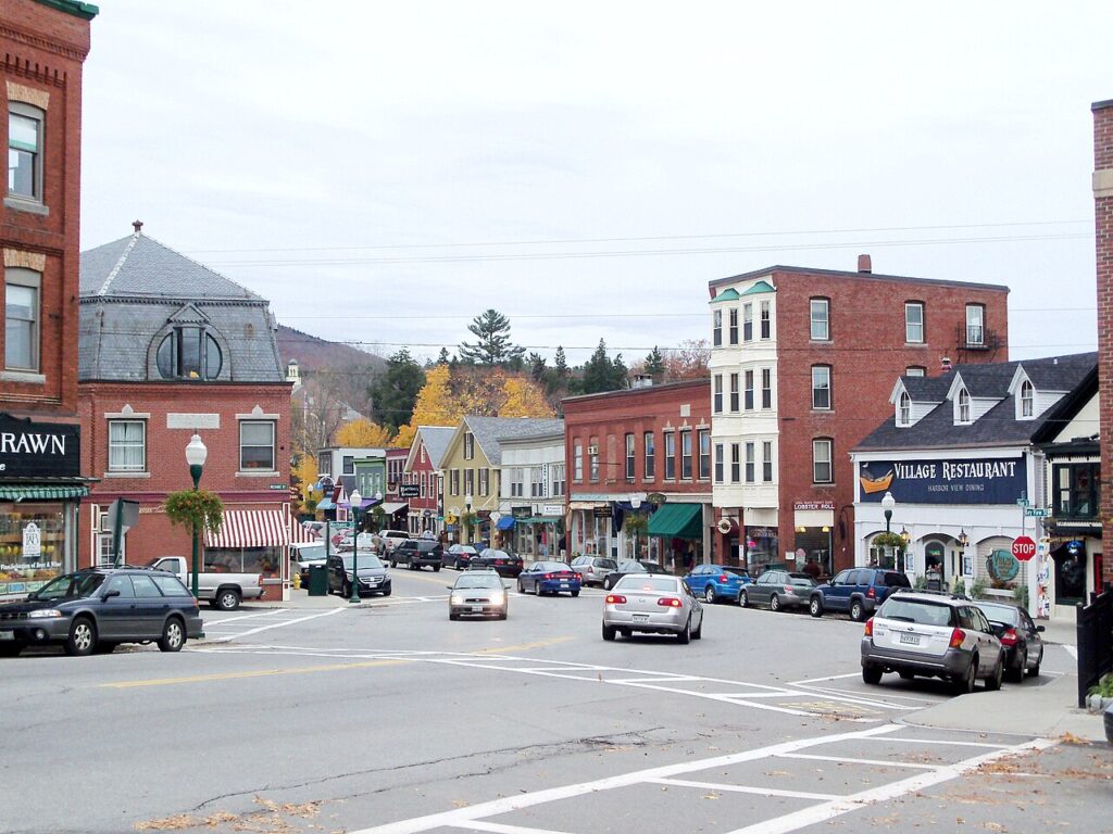 Cars driving through the charming downtown Camden intersection lined with historic brick storefronts.