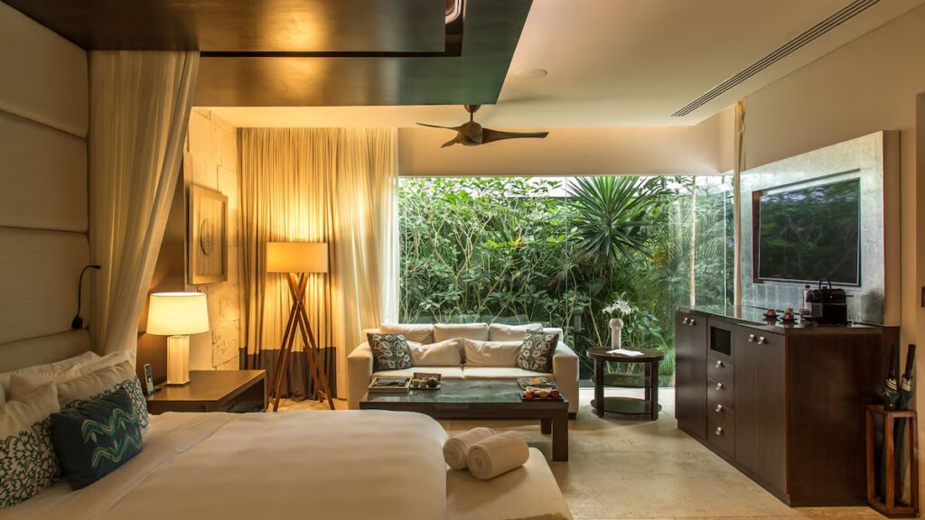 A serene bedroom suite featuring a large window looking out onto lush green foliage at Chablé Yucatán.