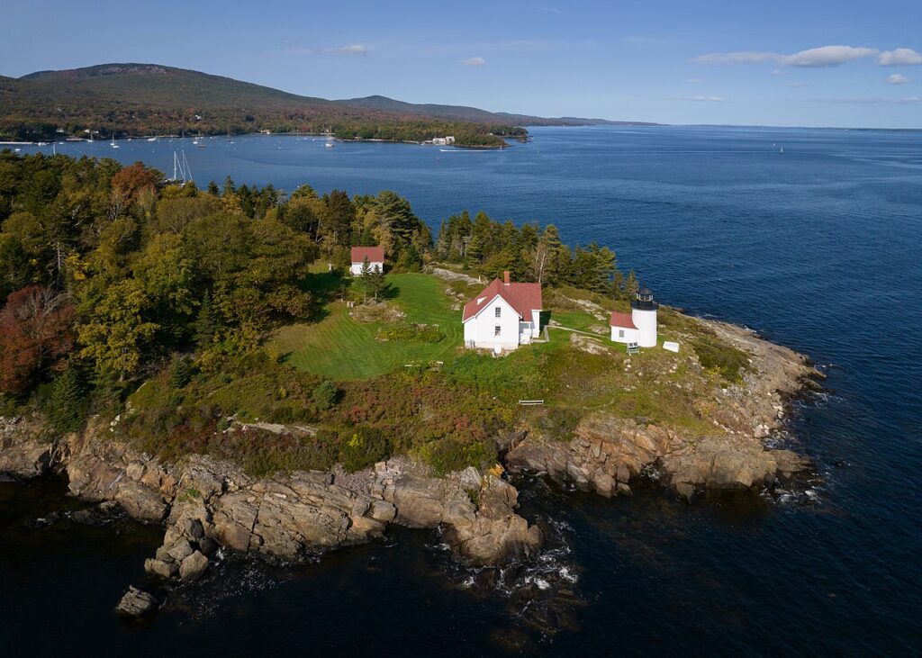 The white Curtis Island Lighthouse and keeper's house perched on a rocky, tree-covered island.
