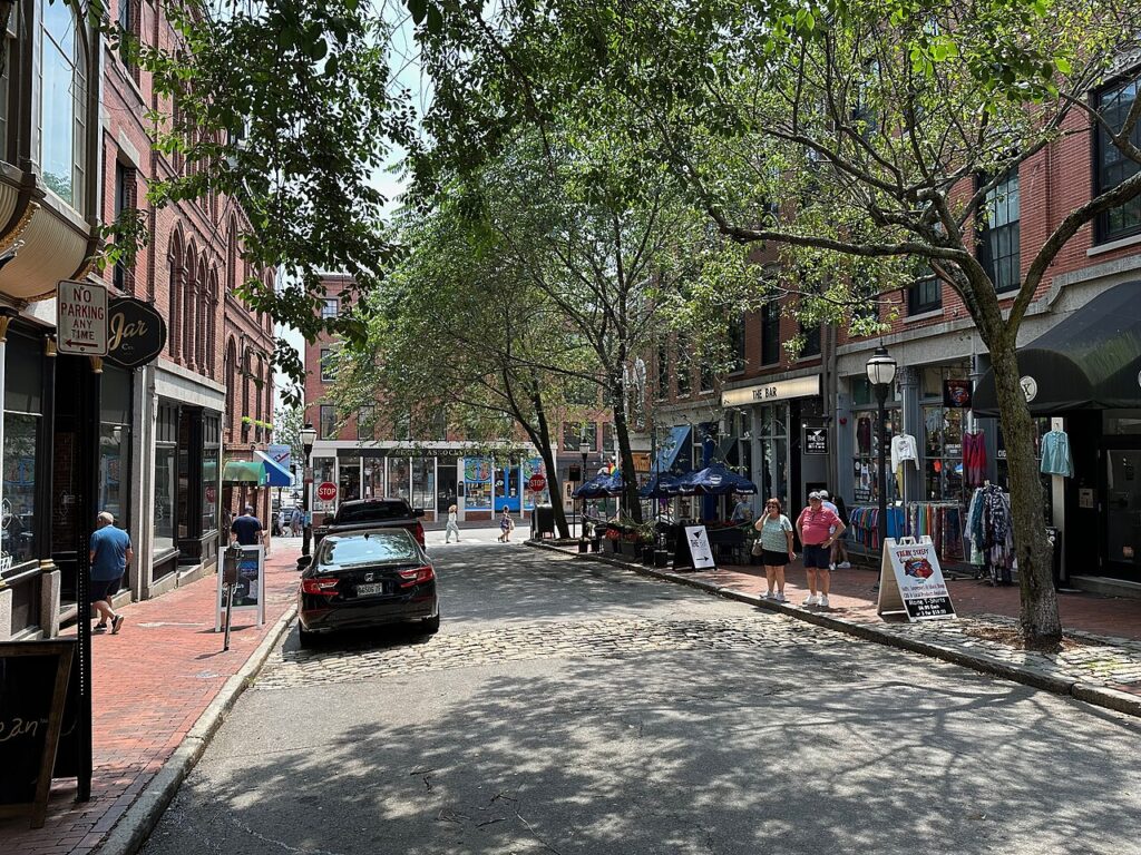 People walking along the charming, tree-lined cobblestone path of Exchange Street in the Old Port. 