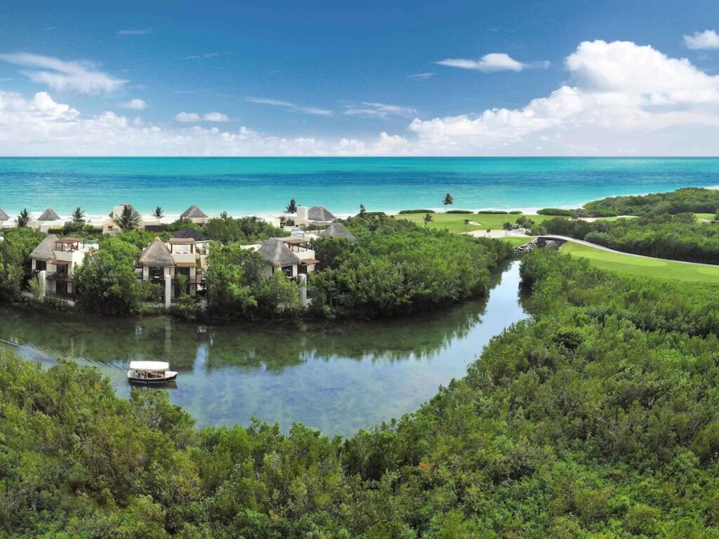 Aerial view of lush mangroves and a small boat navigating waterways at Fairmont Mayakoba. 