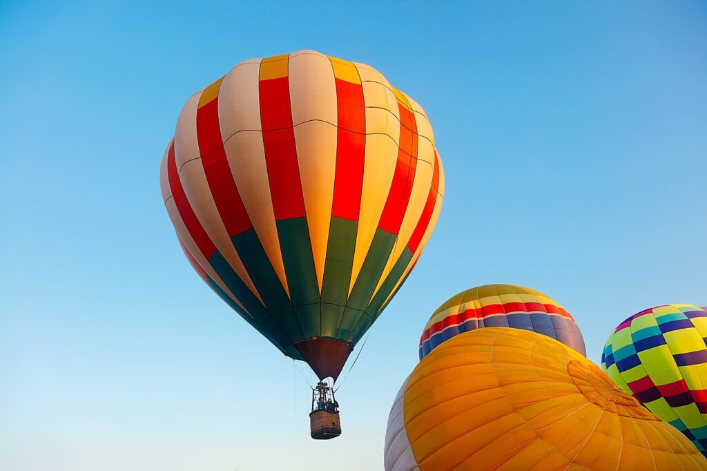 Brightly colored hot air balloons floating in a clear blue summer sky.