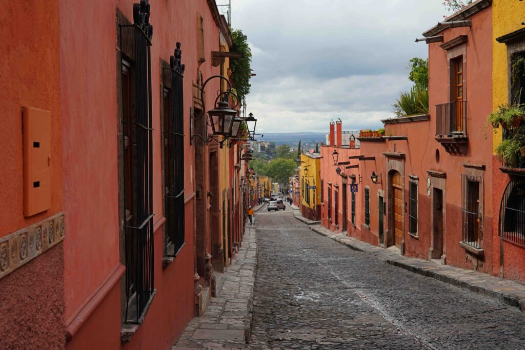 A charming, narrow cobblestone street lined with vibrant red and orange colonial buildings in San Miguel de Allende.