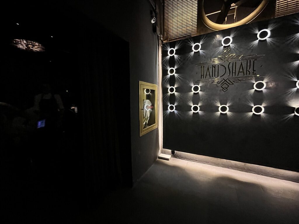The dark and mysterious entrance to Handshake Speakeasy, featuring a wall decorated with illuminated star accents. 