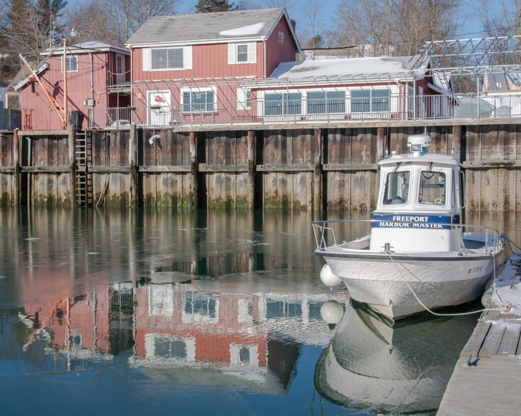 A small white boat labeled "Freeport Harbor Master" docked in front of a waterfront building.