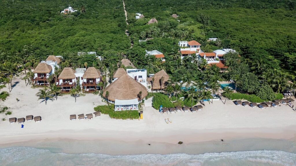 An aerial view of palm-thatched buildings set directly on the white sand beach at La Valise Tulum.