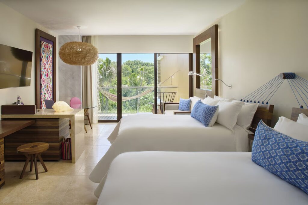 Comfortable hotel room with two beds and blue accent pillows at Hotel Xcaret Arte. 
