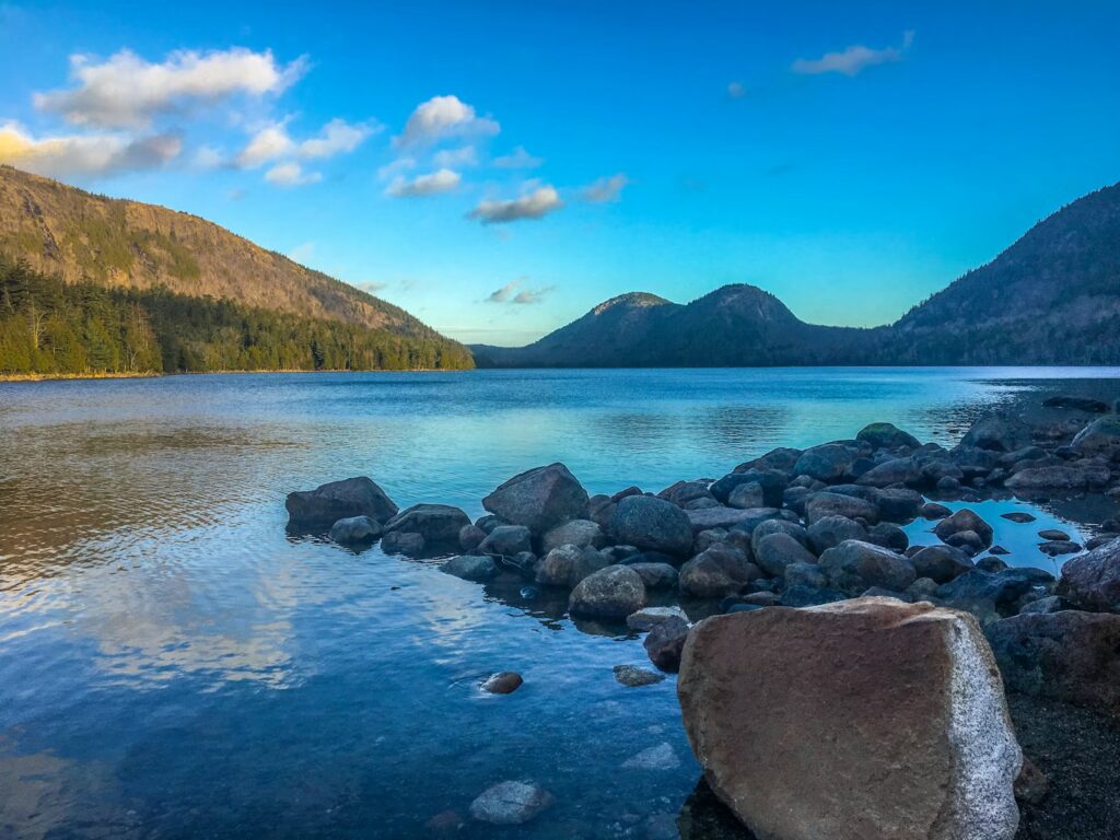 A calm, clear freshwater lake surrounded by rounded mountains and rocky shoreline.