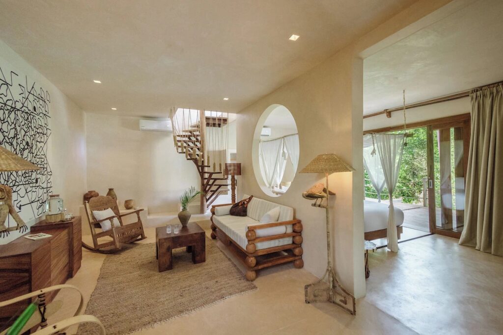 A rustic, jungle-chic hotel room with a circular window and wooden rocking chair at La Valise Tulum.