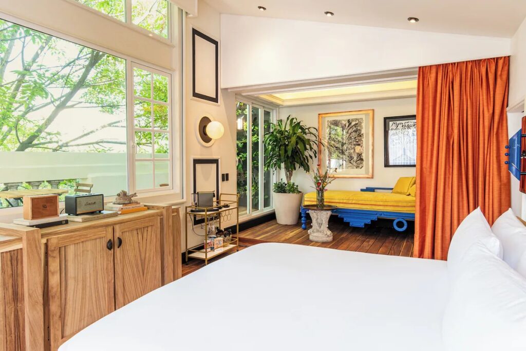 A brightly lit bedroom suite with an orange curtain room divider and yellow daybed at La Valise Mexico City.