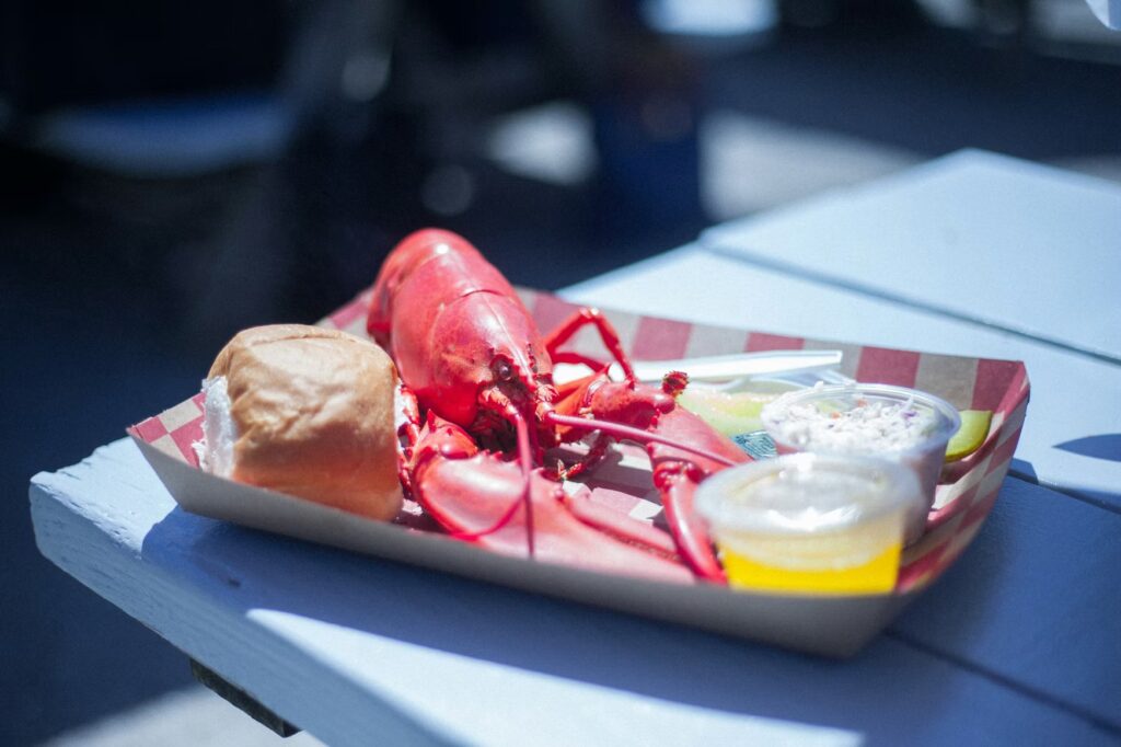 A bright red, freshly cooked lobster served with a roll and melted butter on a paper tray.