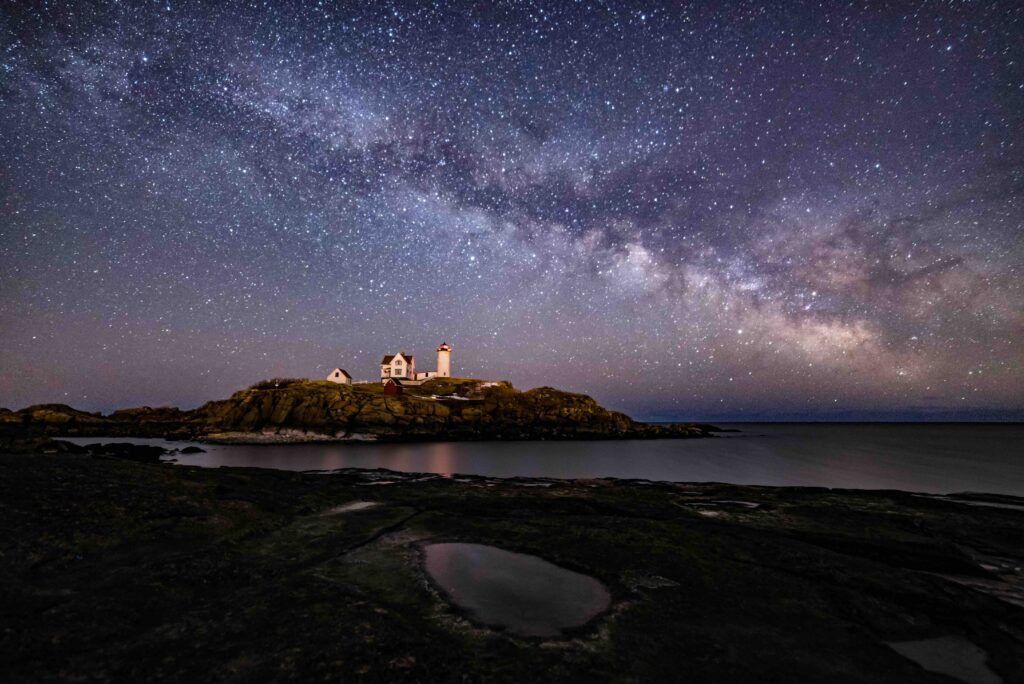 The bright Milky Way galaxy glowing brilliantly in the dark night sky above a coastal lighthouse.