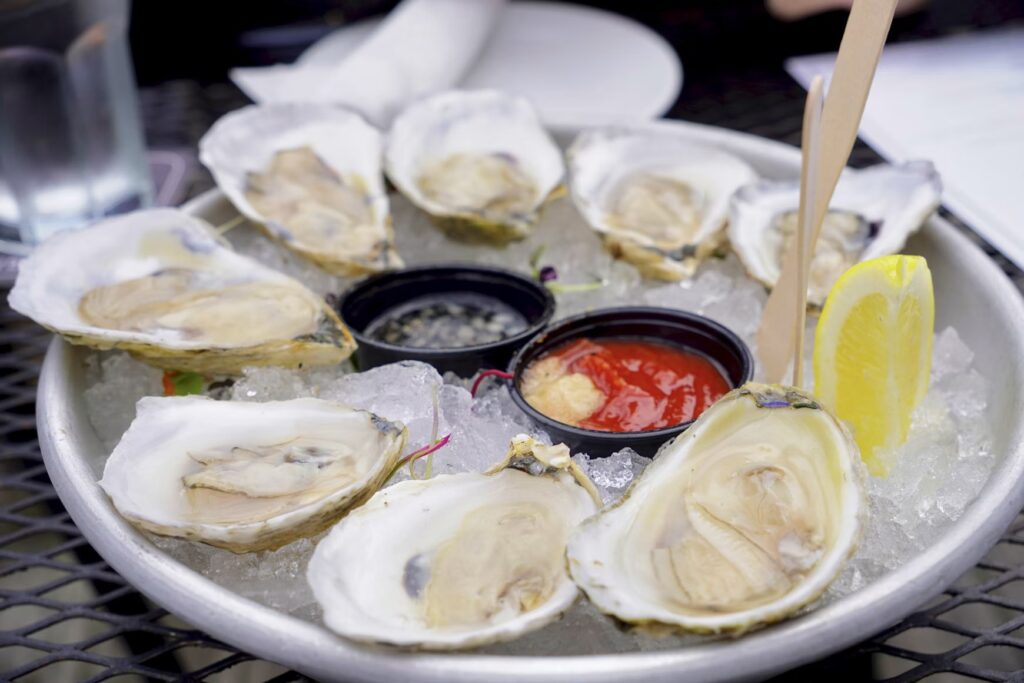 A dozen fresh oysters served on a bed of ice with lemon and cocktail sauce dipping bowls.