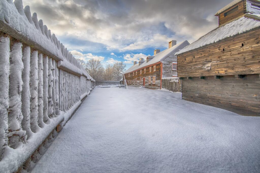 A historic wooden fort and stockade fence covered in a thick layer of winter snow.