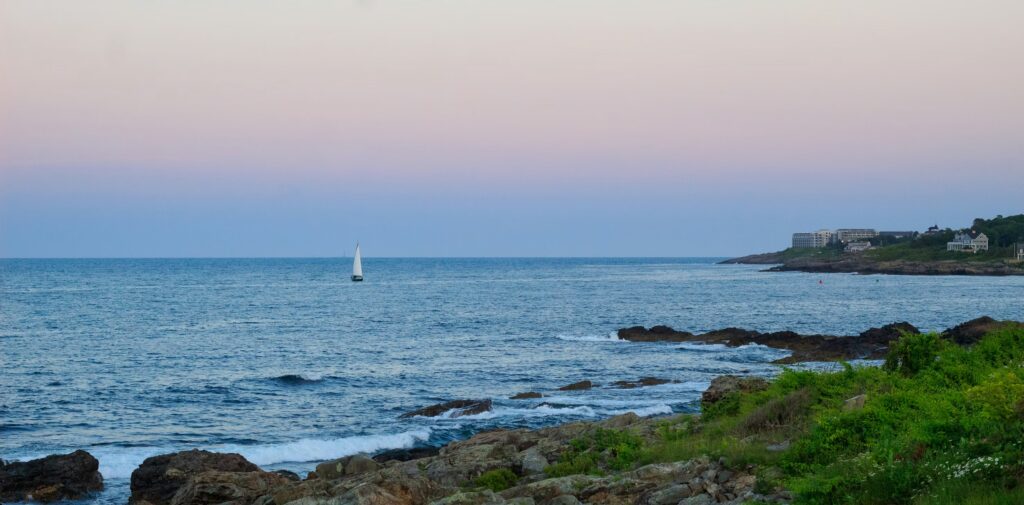 12 Best Things to Do in Ogunquit, Maine (Cliffs, Coves & Itineraries) A sailboat cruising along the rocky coastal waters, representing best things to do in Ogunquit Maine.