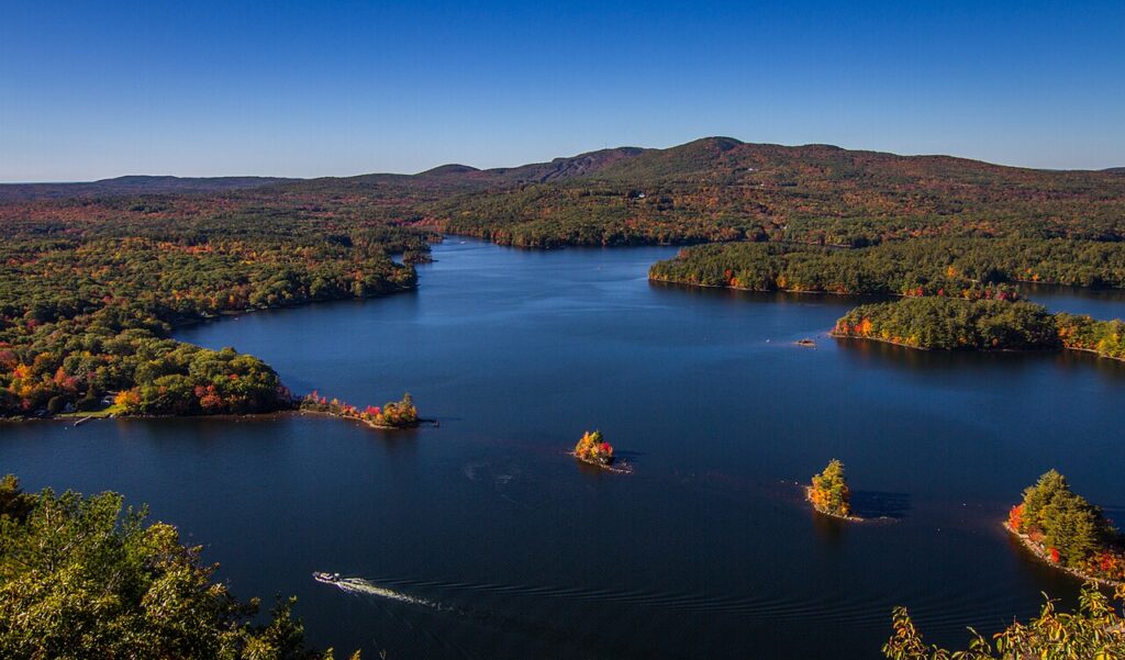 Aerial view of the deep blue waters of Megunticook Lake surrounded by colorful autumn forest foliage.