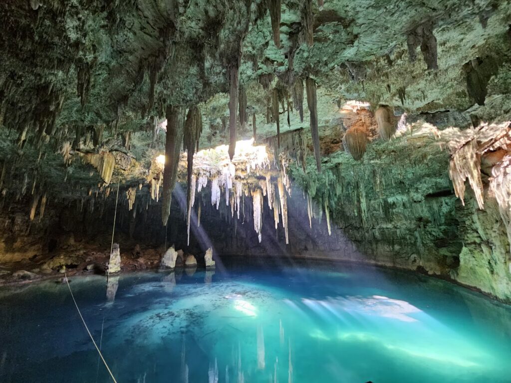 Sunlight beams piercing the crystal-clear water of a cavern with stalactites in the Mexican Cenotes. 