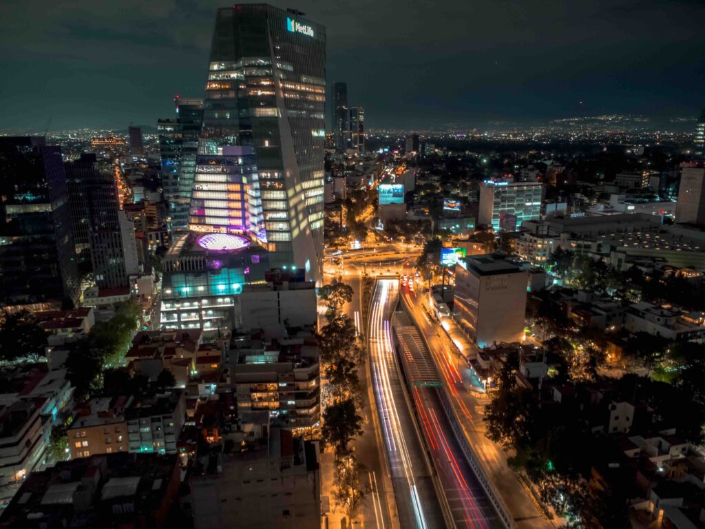 An expansive aerial view of the illuminated Mexico City skyline and busy highways stretching into the night. 