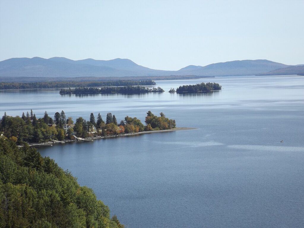 A calm blue lake dotted with small islands and pine forests at Moosehead Lake, Maine.