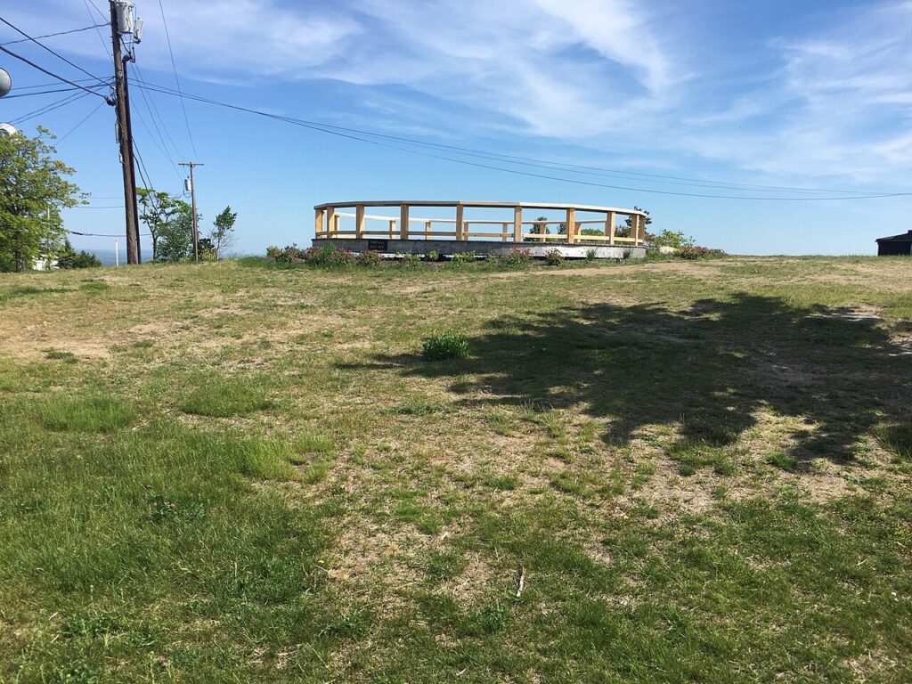 A circular wooden observation deck sitting on a grassy hilltop at the summit of Mount Agamenticus in York, Maine.
