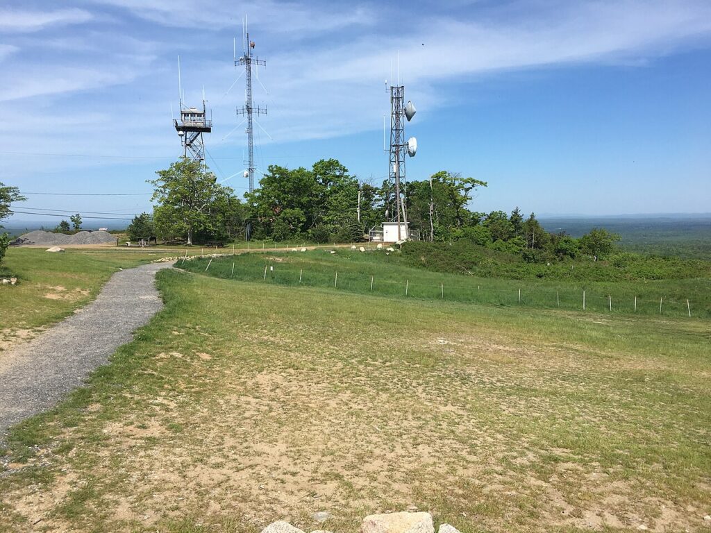 Tall communication towers standing near a gravel path on the scenic grassy summit of Mount Agamenticus in York.