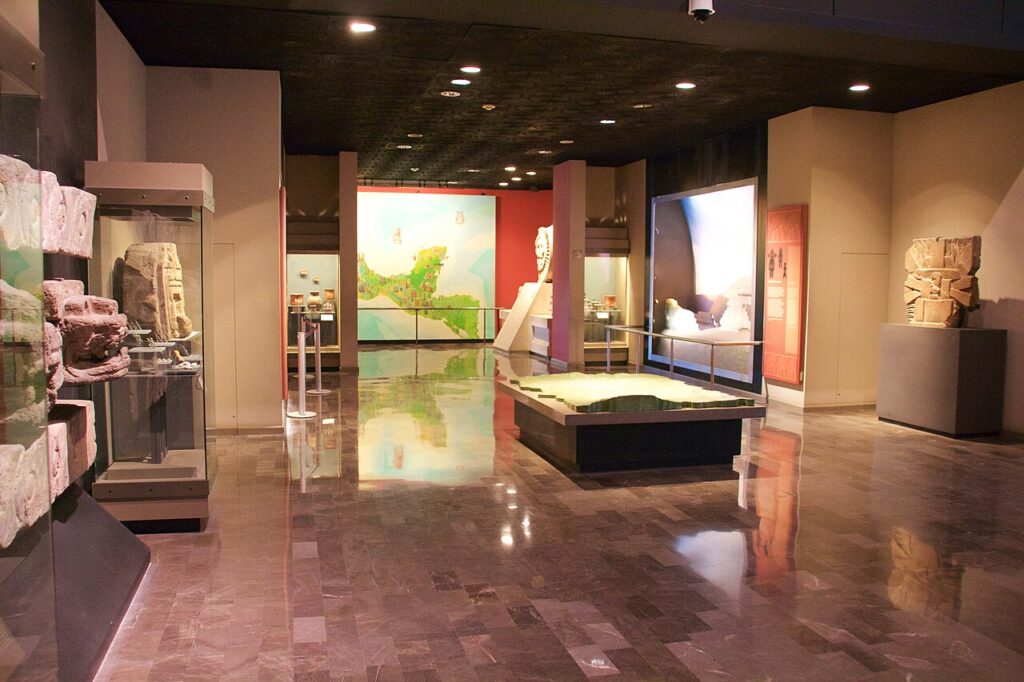 An interior exhibit hall featuring ancient stone artifacts and murals at the National Museum of Anthropology.