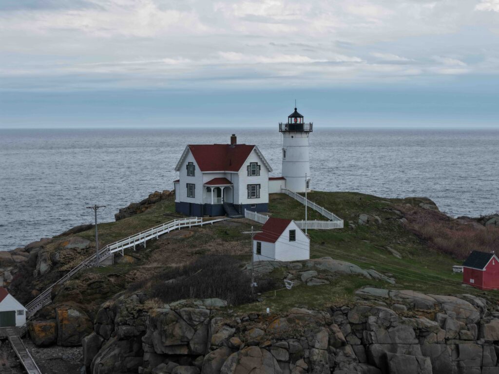 Nubble Lighthouse perched on a rugged, rocky island surrounded by the ocean on a cloudy day in Cape Neddick, York.