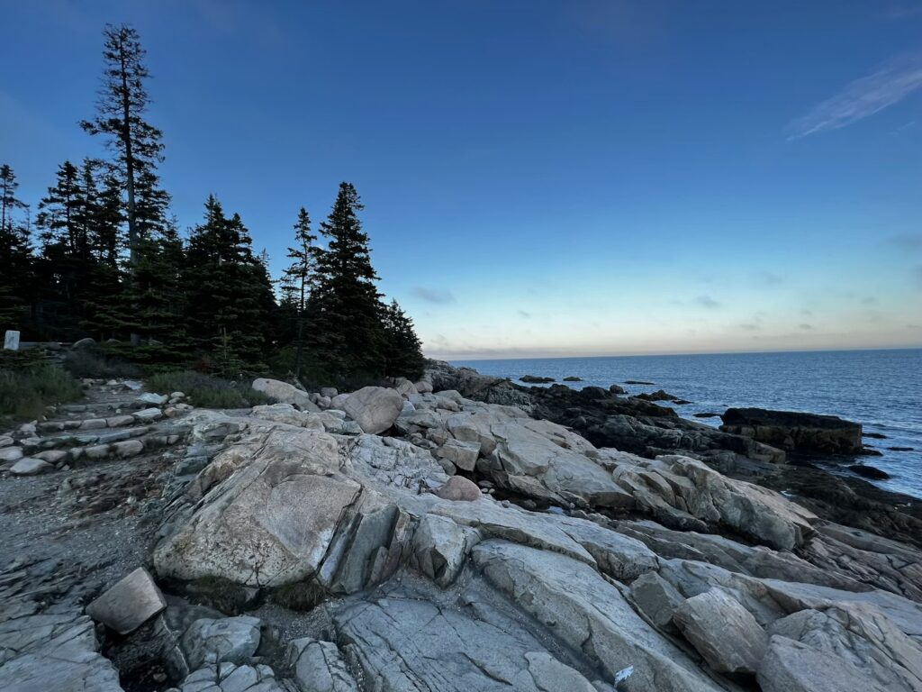Smooth, wave-washed pink granite rocks along the shoreline facing the calm ocean at dusk.