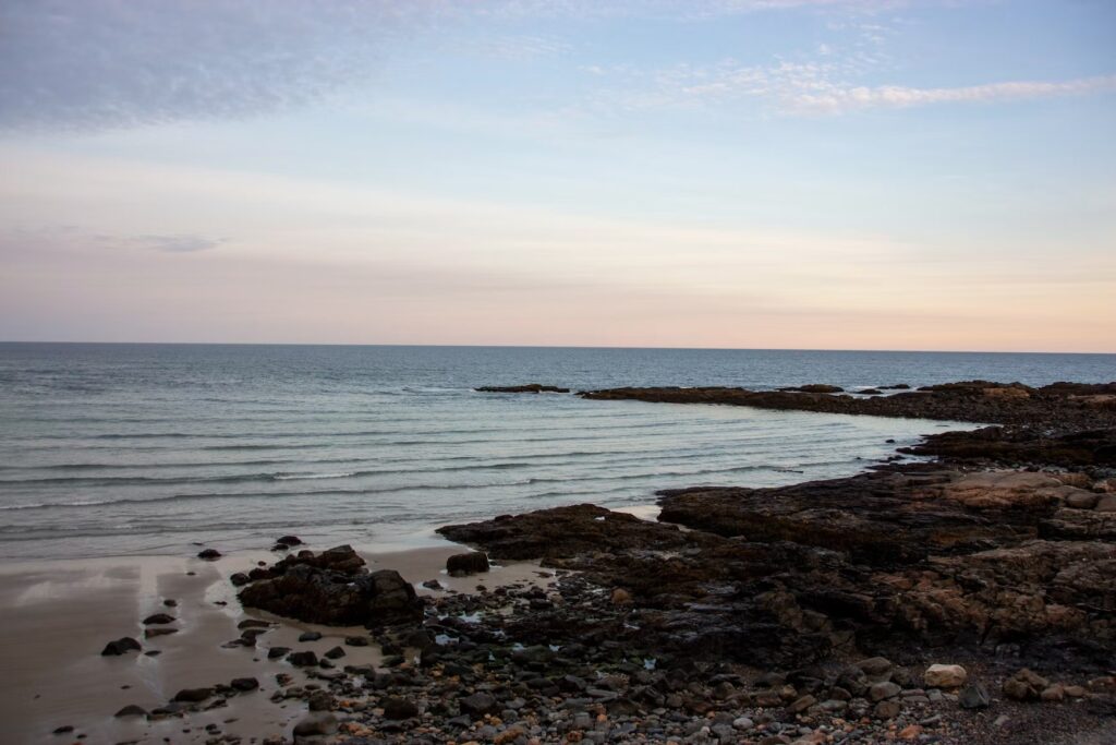 Rocky tide pools and calm ocean waters visible along the scenic shoreline of Ogunquit Beach, Maine at dusk.
