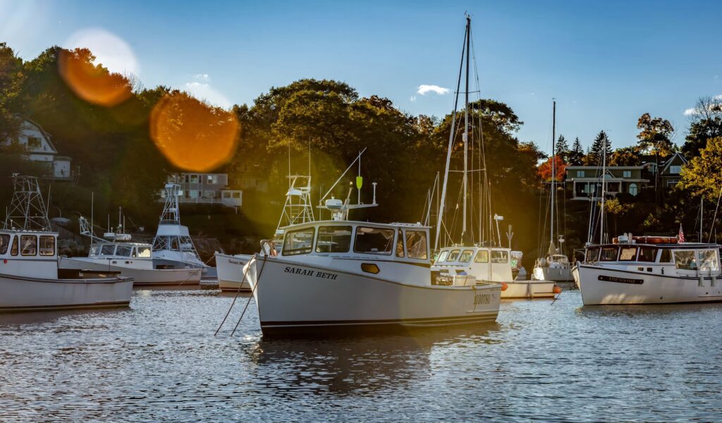 Several boats anchored in the calm waters of Perkins Cove harbor during a golden sunset in Ogunquit, Maine.