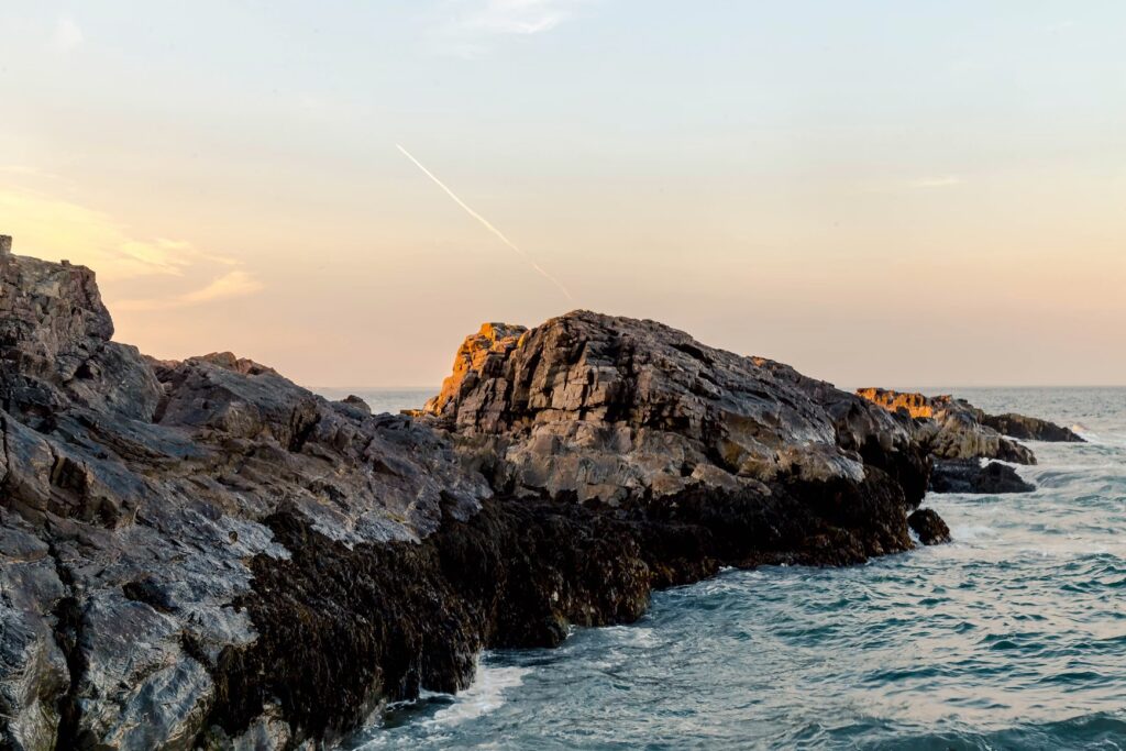 Jagged granite rocks covered in dark seaweed glowing under the sunset light in Ogunquit, Maine.