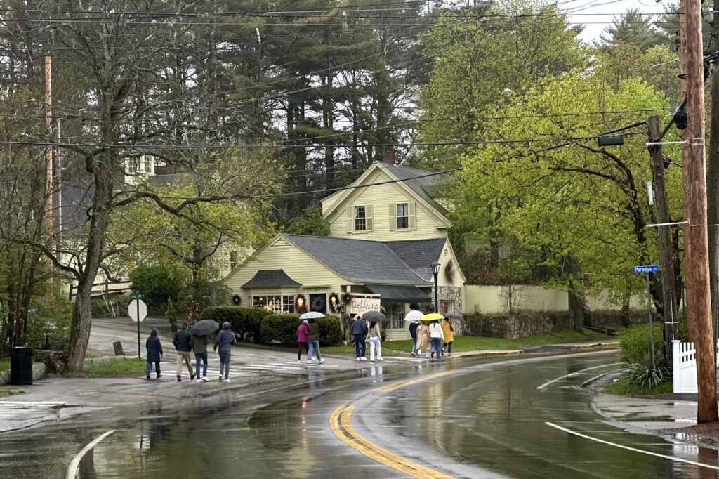 People walking with umbrellas along the charming, tree-lined streets of downtown Ogunquit, Maine on a rainy day.