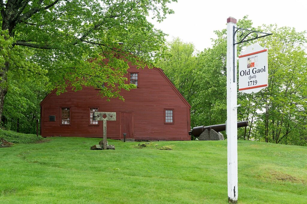 The historic red wooden exterior and white sign of the colonial-era Old Gaol museum located in York Village, Maine.