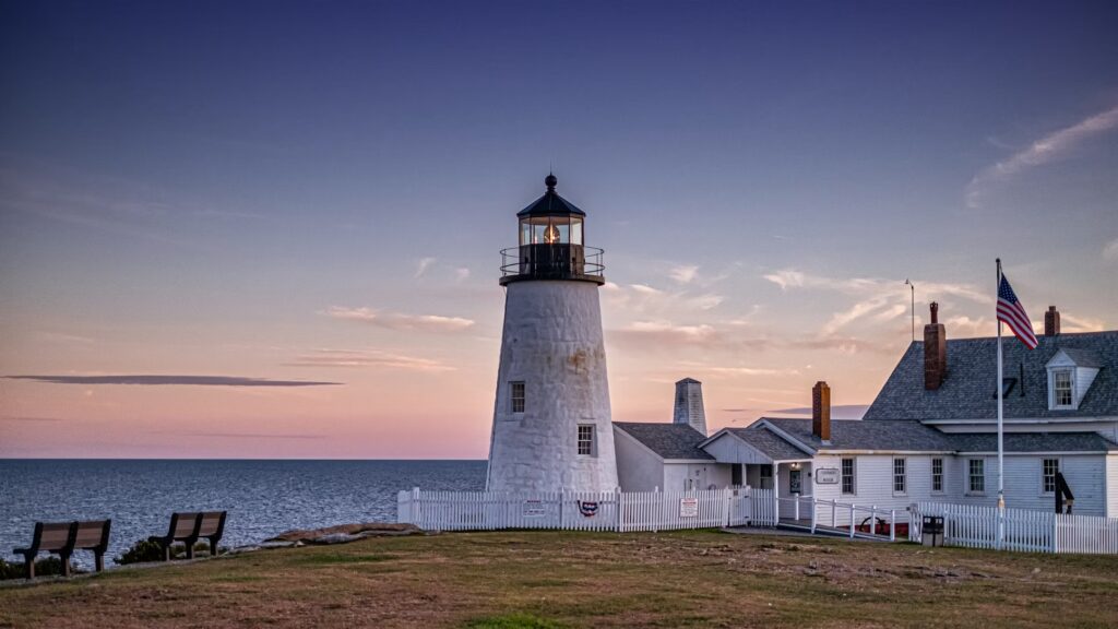 Pemaquid Point Light and the keeper's house sitting on a grassy coastal bluff under a sunset sky.