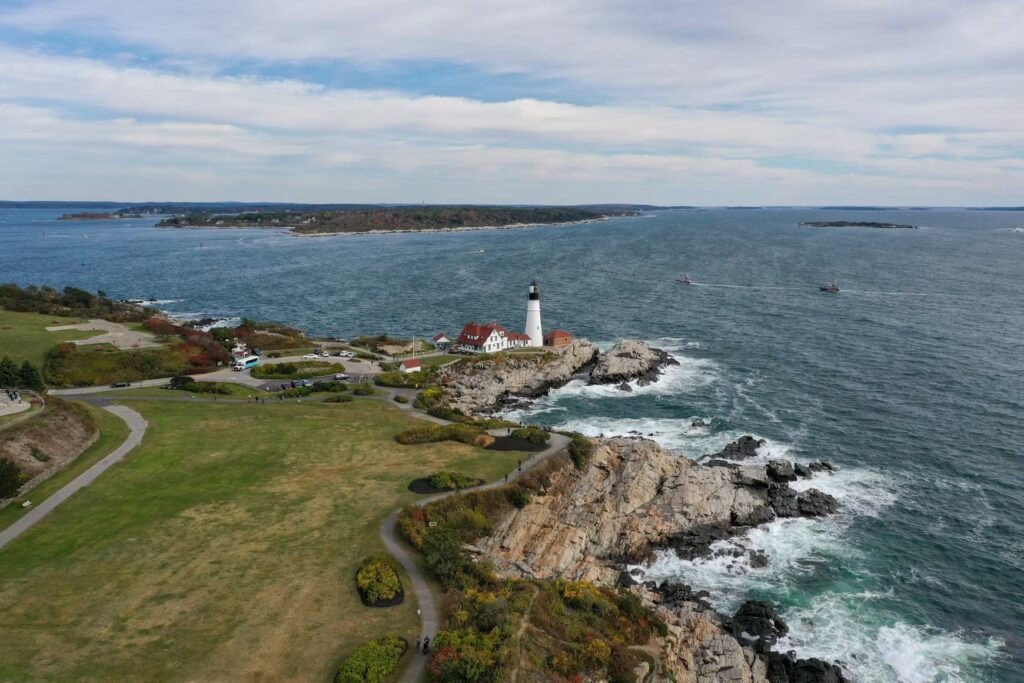 Aerial view of a historic lighthouse perched on a rugged, rocky peninsula in Cape Elizabeth. 