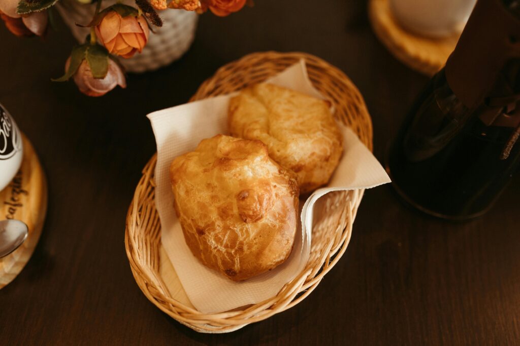 Two golden, hollow popover pastries served in a small woven basket on a napkin.