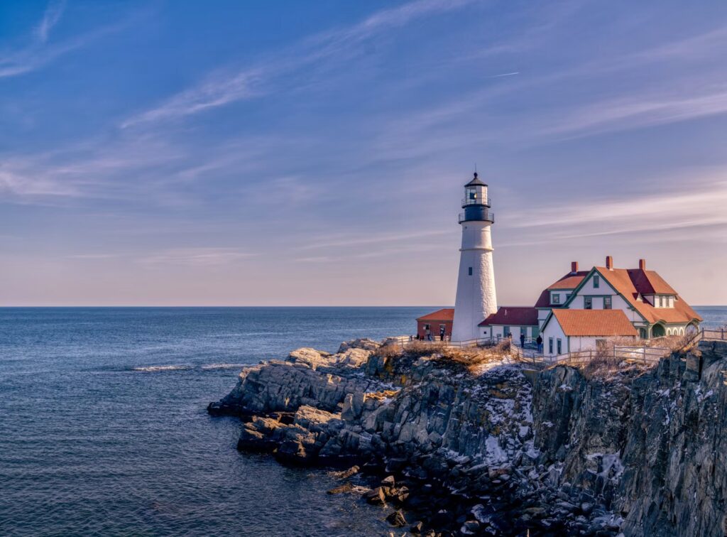 Portland Head Light perched on a rugged, rocky cliff edge against the blue ocean.