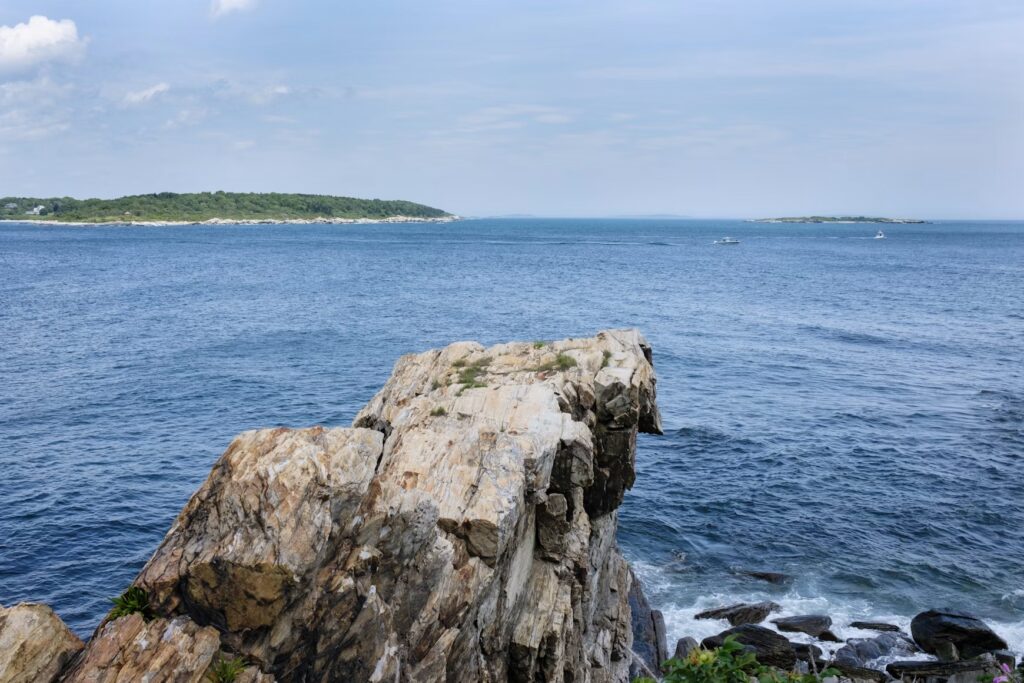 Ocean waves crashing against a massive, weathered granite rock formation along the Maine coastline. 