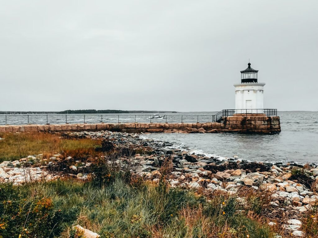 A small white lighthouse sitting at the end of a stone breakwater in South Portland, Maine.