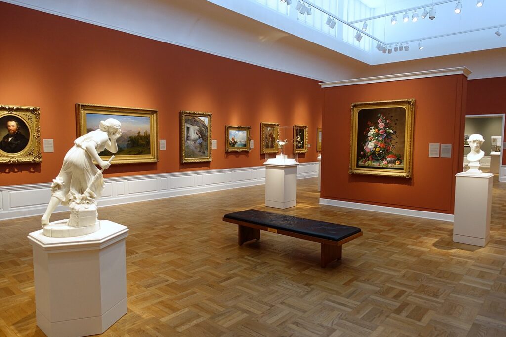 An indoor gallery at an art museum displaying classical paintings and white marble statues.