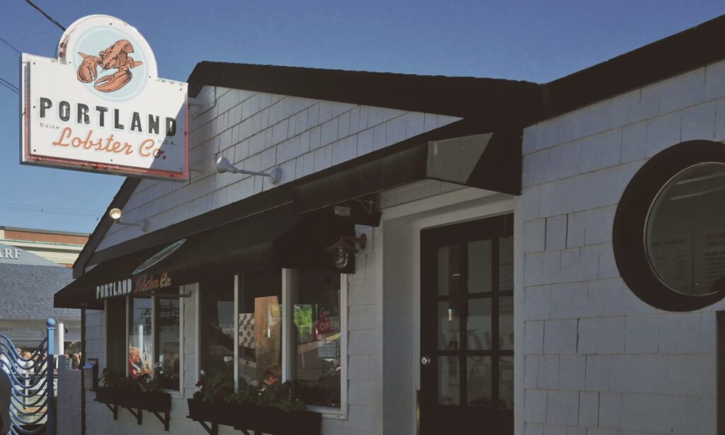 The exterior of the Portland Lobster Co. restaurant, featuring its classic sign with a red lobster. 
