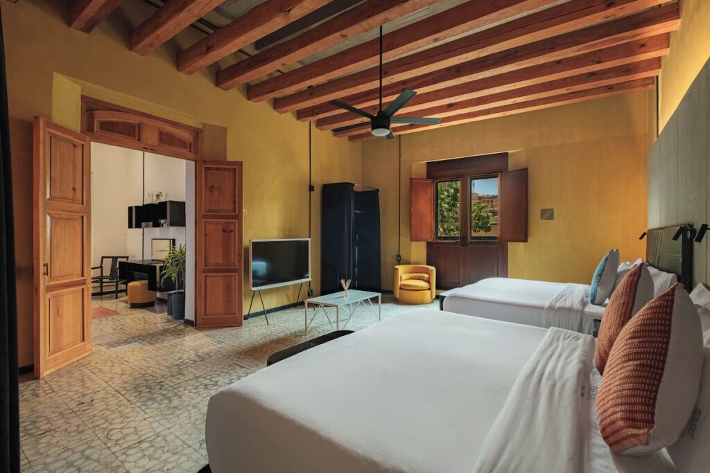 A modern, spacious hotel room with two large beds and warm yellow walls at Pug Seal Oaxaca.